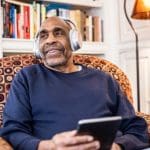 Senior man listening to music on wireless headphones at home