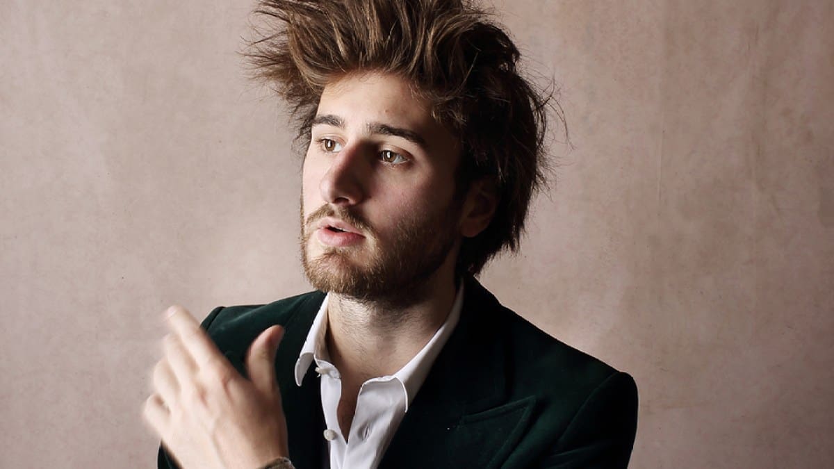 Harpsichordist Jean Rondeau, a white man with tall brown hair and a beard, wearing a dark green jacket, white shirt, and silver bracelets, looks off to the left of the camera.