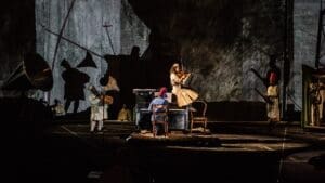 A photo of a scene from William Kentridge's The Head and The Load, the actors playing several instruments against a multimedia backdrop.