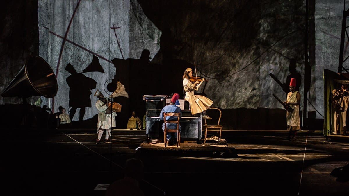 A photo of a scene from William Kentridge's The Head and The Load, the actors playing several instruments against a multimedia backdrop.