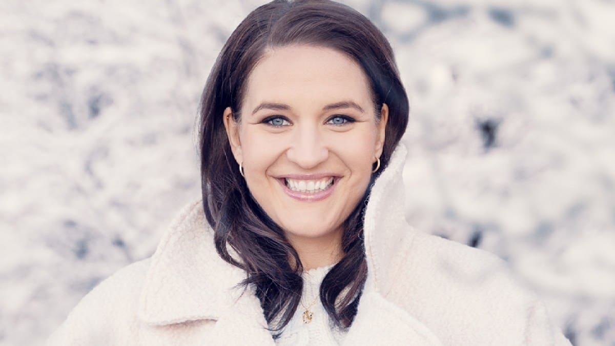 Soprano Lise Davidsen, a white woman with long brown hair dressed in a white sweater and white fleece coat, looks toward the camera against a snowy background