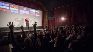 A Doc Stories audience raises their hands during a filmmaker conversation in a movie theater.