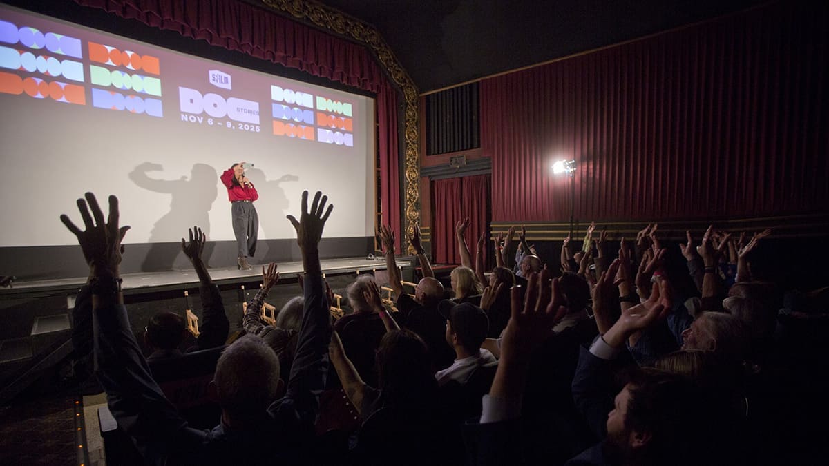 A Doc Stories audience raises their hands during a filmmaker conversation in a movie theater.