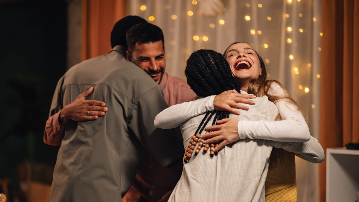 Four people embrace in a close group hug.