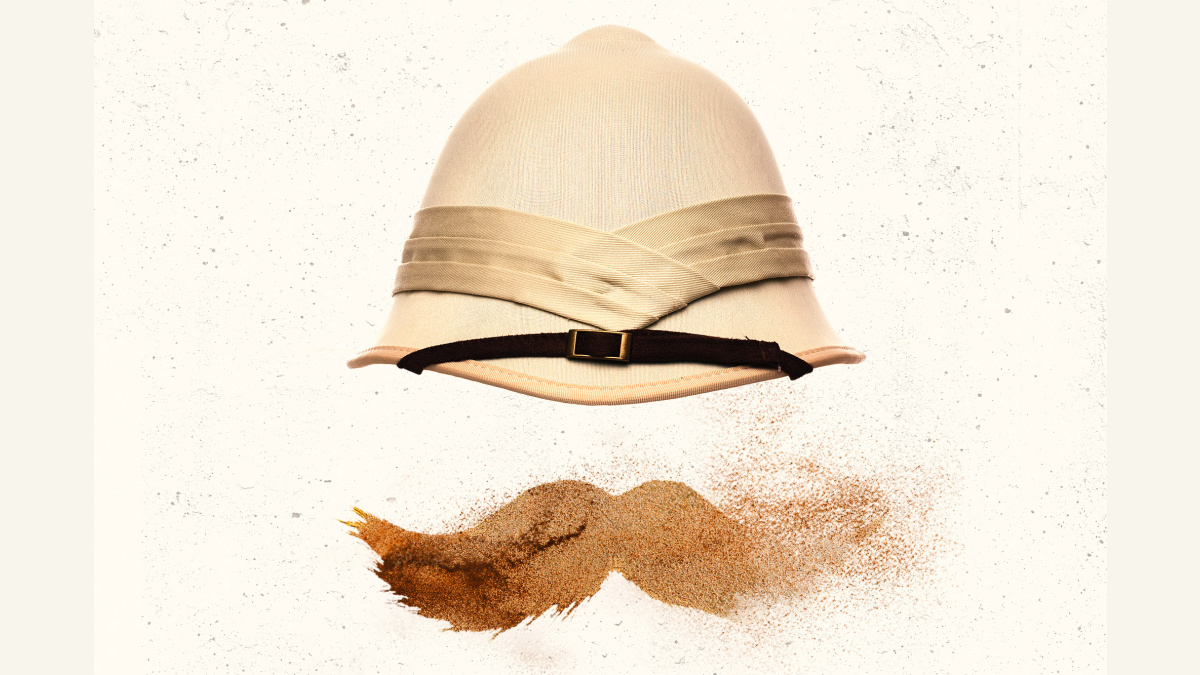 A pith helmet sits above a moustache made of sand on a pale background.