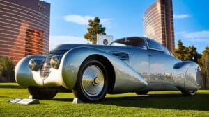 A silver classic car on the lawn with Wynn and Encore towers in the background