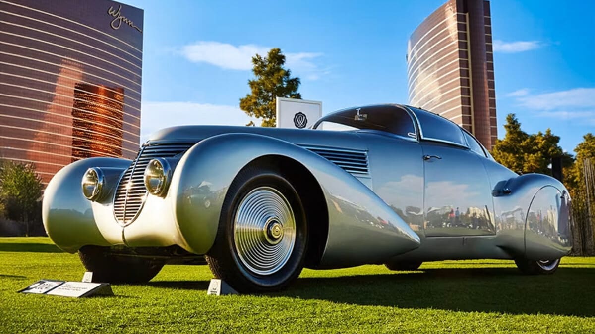A silver classic car on the lawn with Wynn and Encore towers in the background