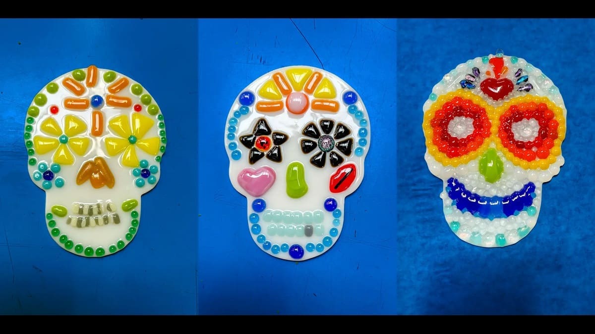 Three colorful fused-glass sugar skulls on a blue surface
