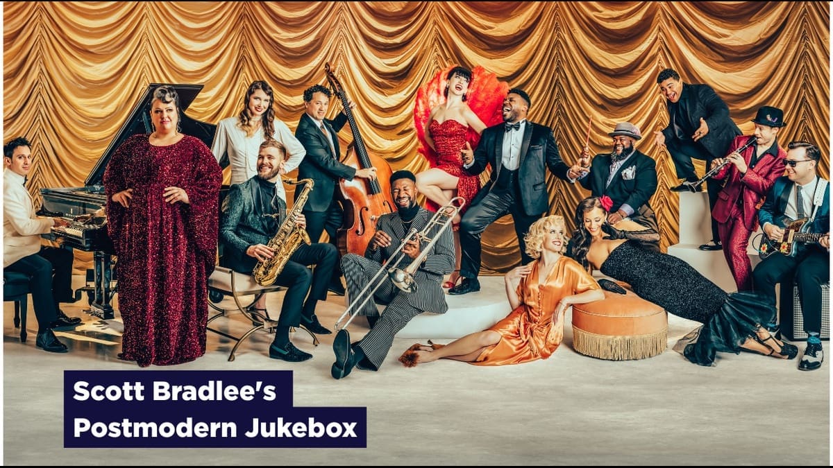Scott Bradlee's Postmodern Jukebox ensemble posed in front of gold curtains.