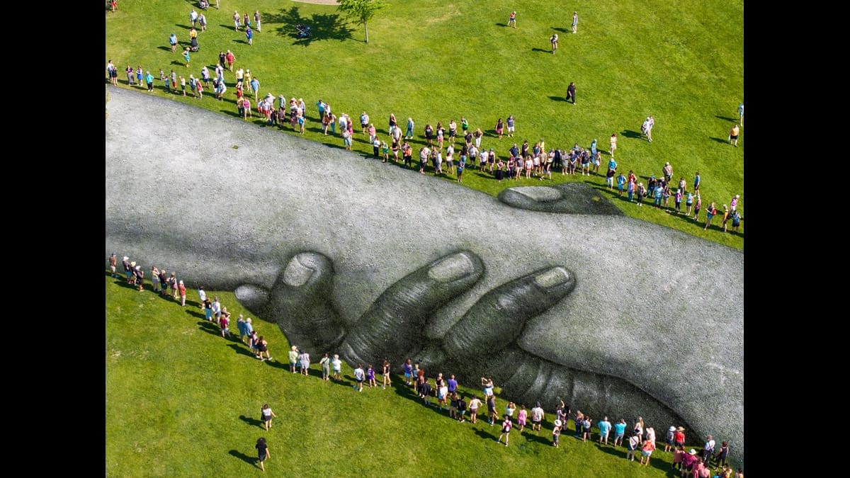 People form a human chain around Saype’s large artwork of interlocking hands.