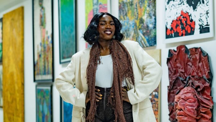 Black woman posing in a contemporary art gallery surrounded by colorful artwork.