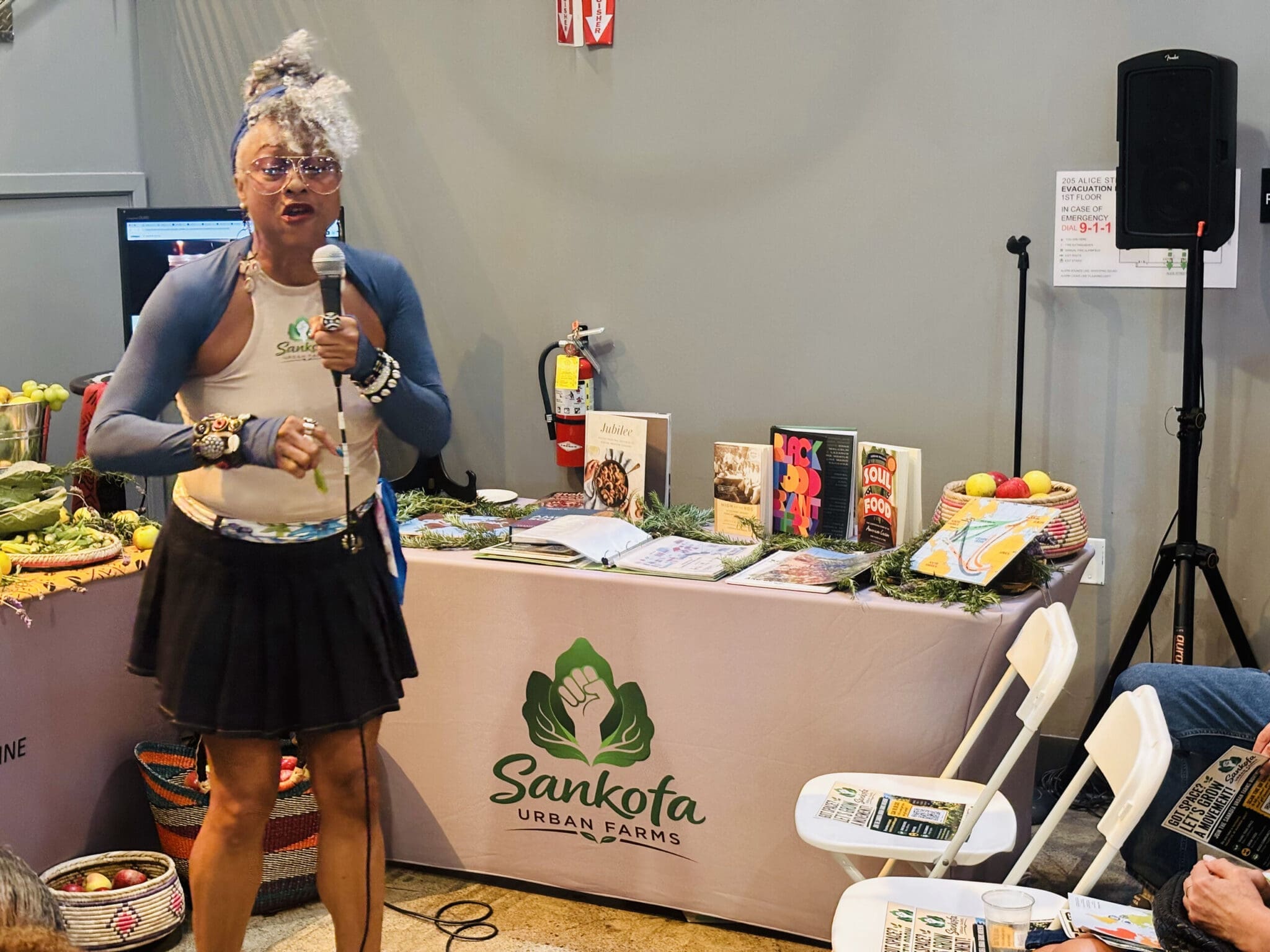 A presenter stands at the Sankofa Urban Farms table.