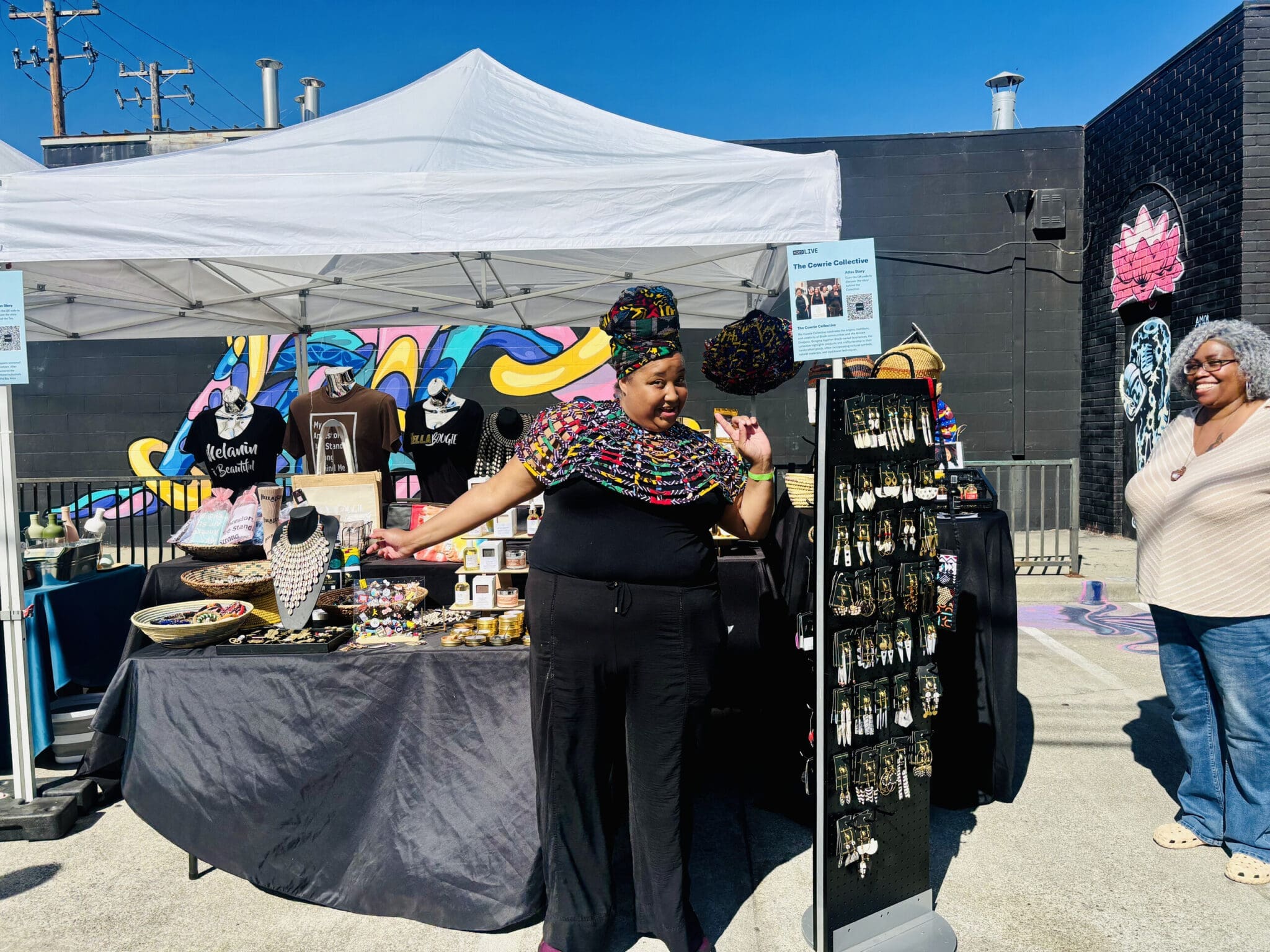 A vendor stands beside an outdoor jewelry and clothing display.