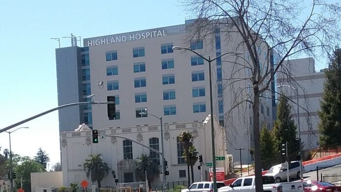 Exterior of Highland Hospital in Oakland, with the hospital name above the windows and a street intersection in front.